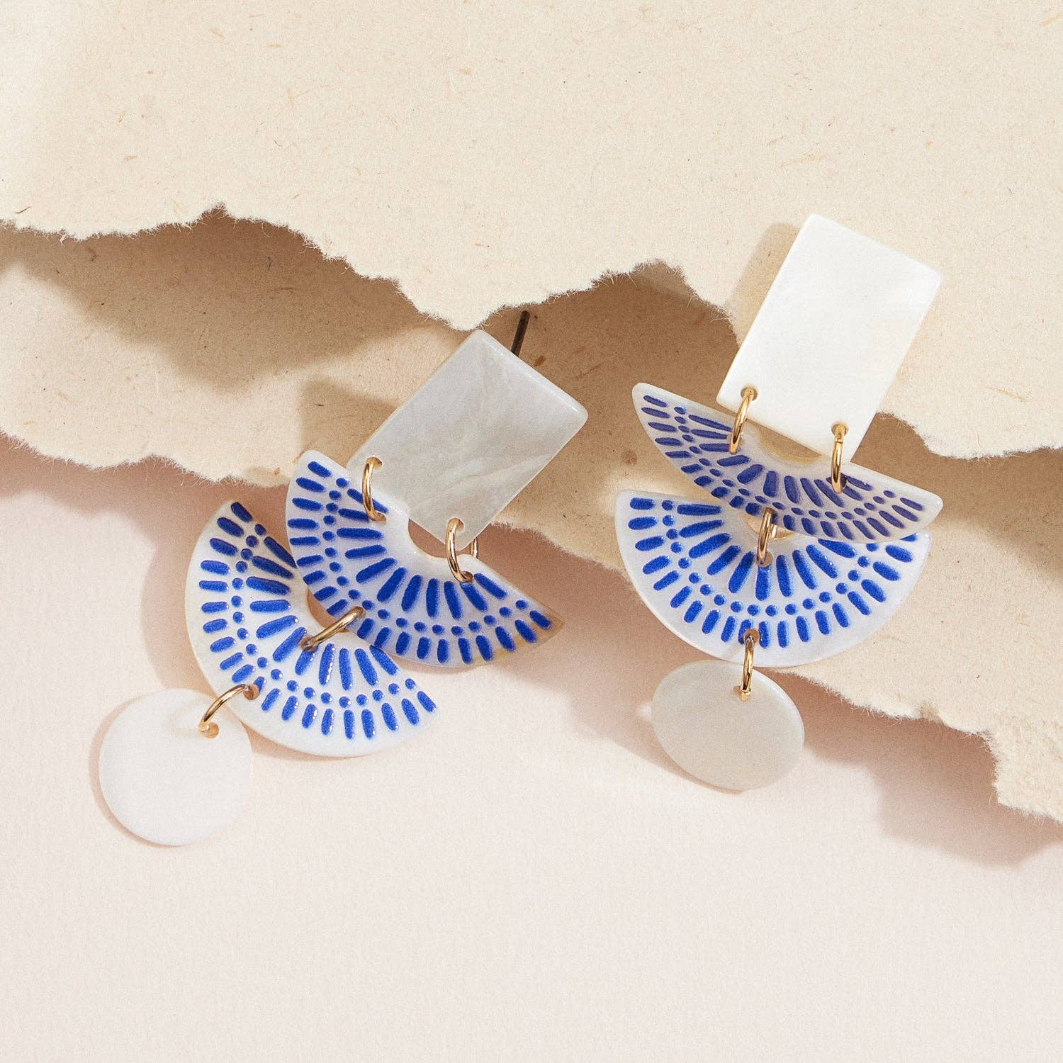 Pair of earrings with blue and white fan-shaped design on a beige background