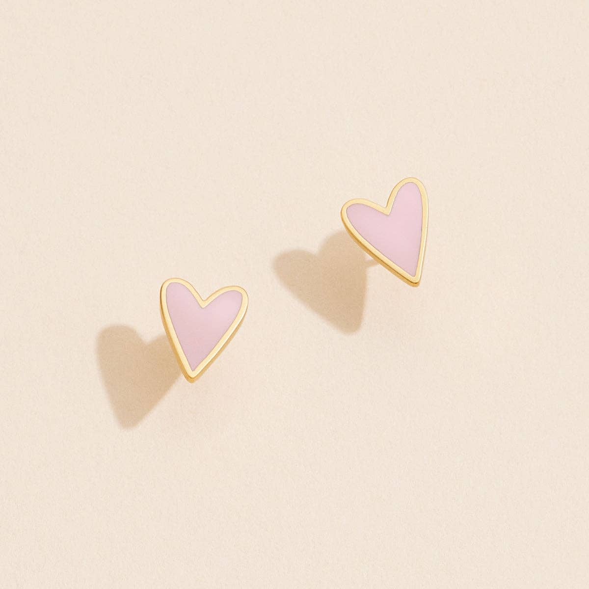 Heart-shaped earrings with pink centers and gold outlines on a beige background