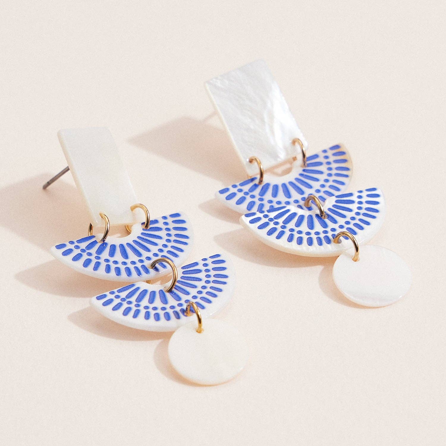 Pair of earrings with blue fan-shaped designs on a beige background