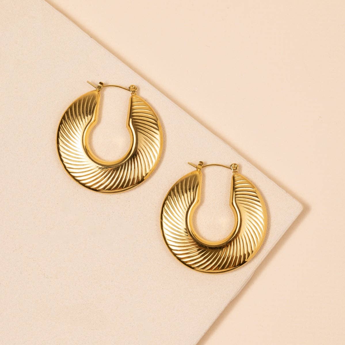 Gold engraved hoop earrings on a beige background