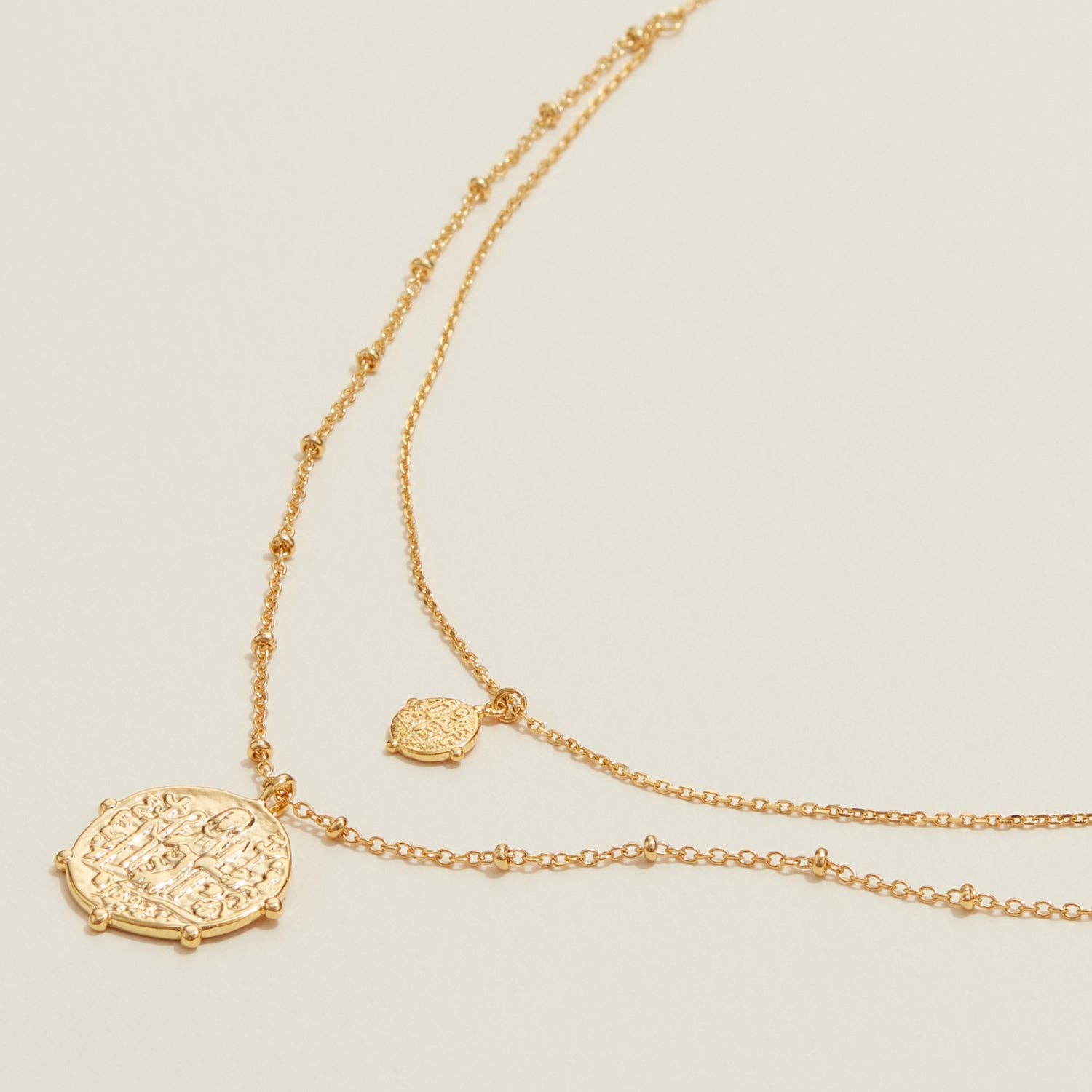 Gold necklace with a decorative pendant on a light beige background