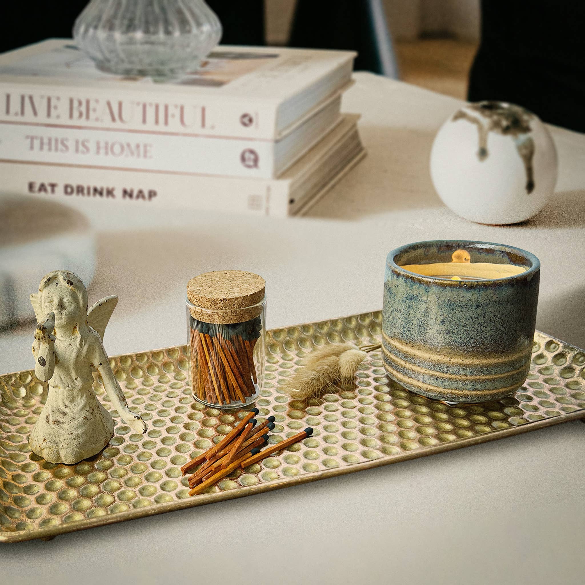 Candle on a decorative tray with books and small items in the background