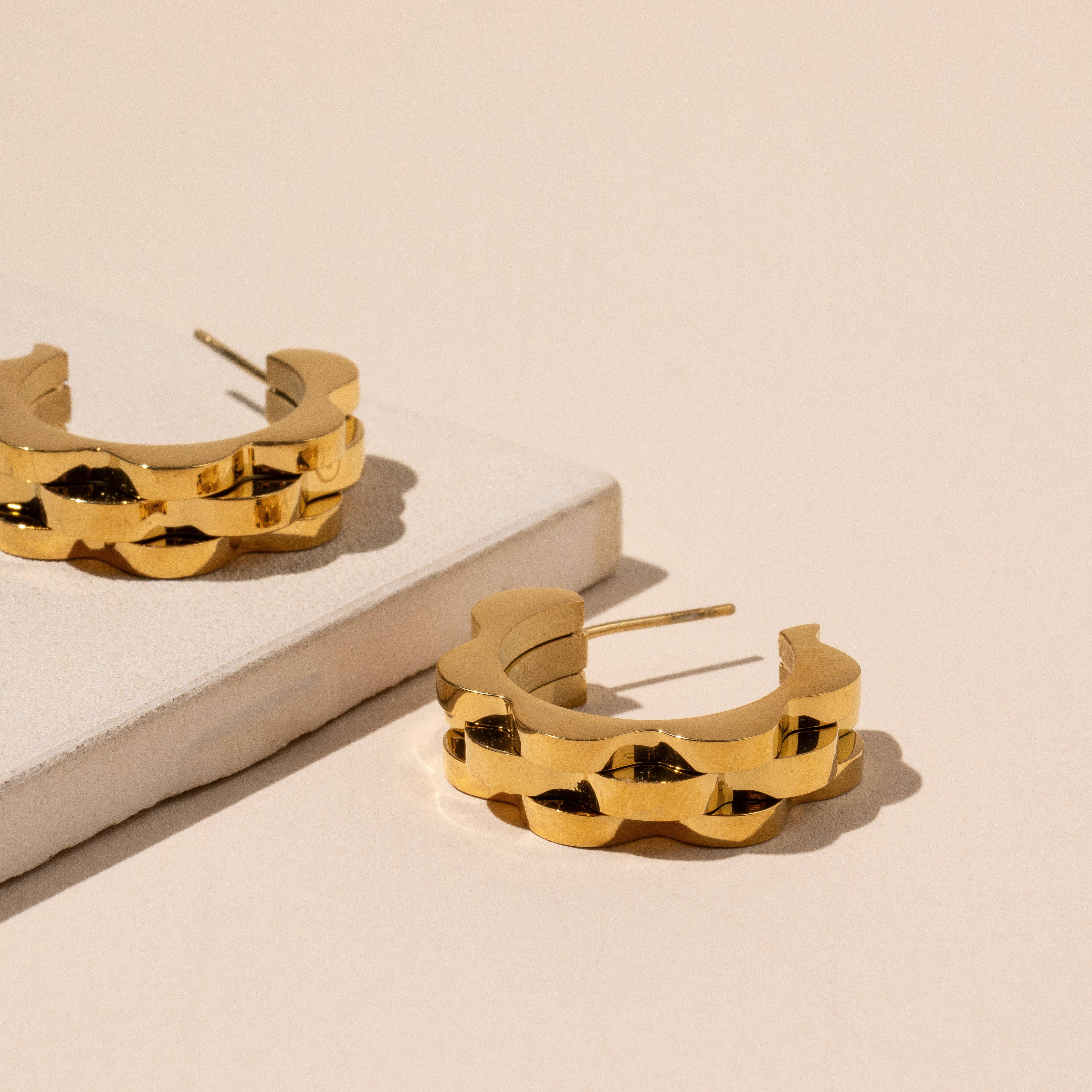Gold watch band earrings on a beige surface