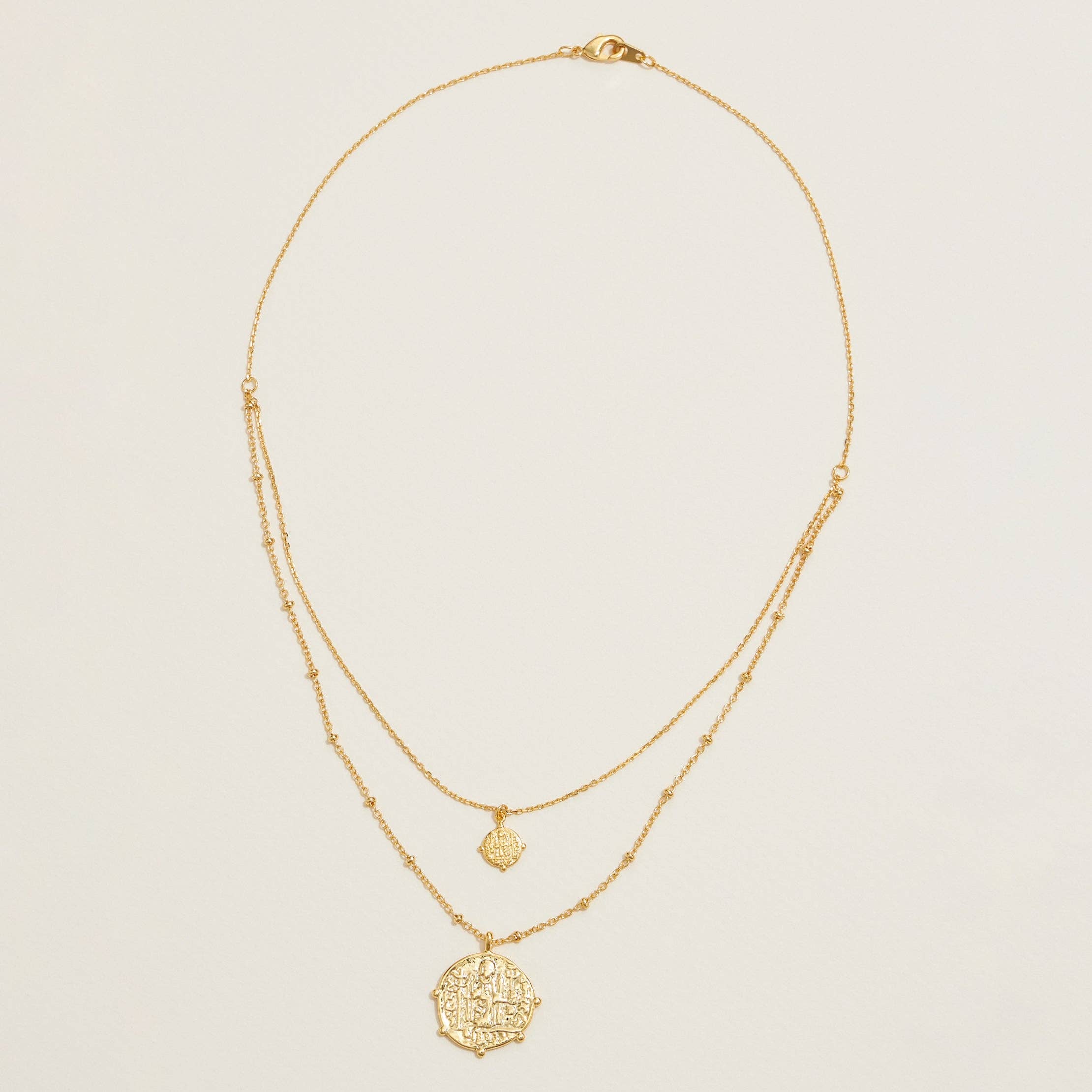 Two gold necklaces with intricate pendants on a light beige background