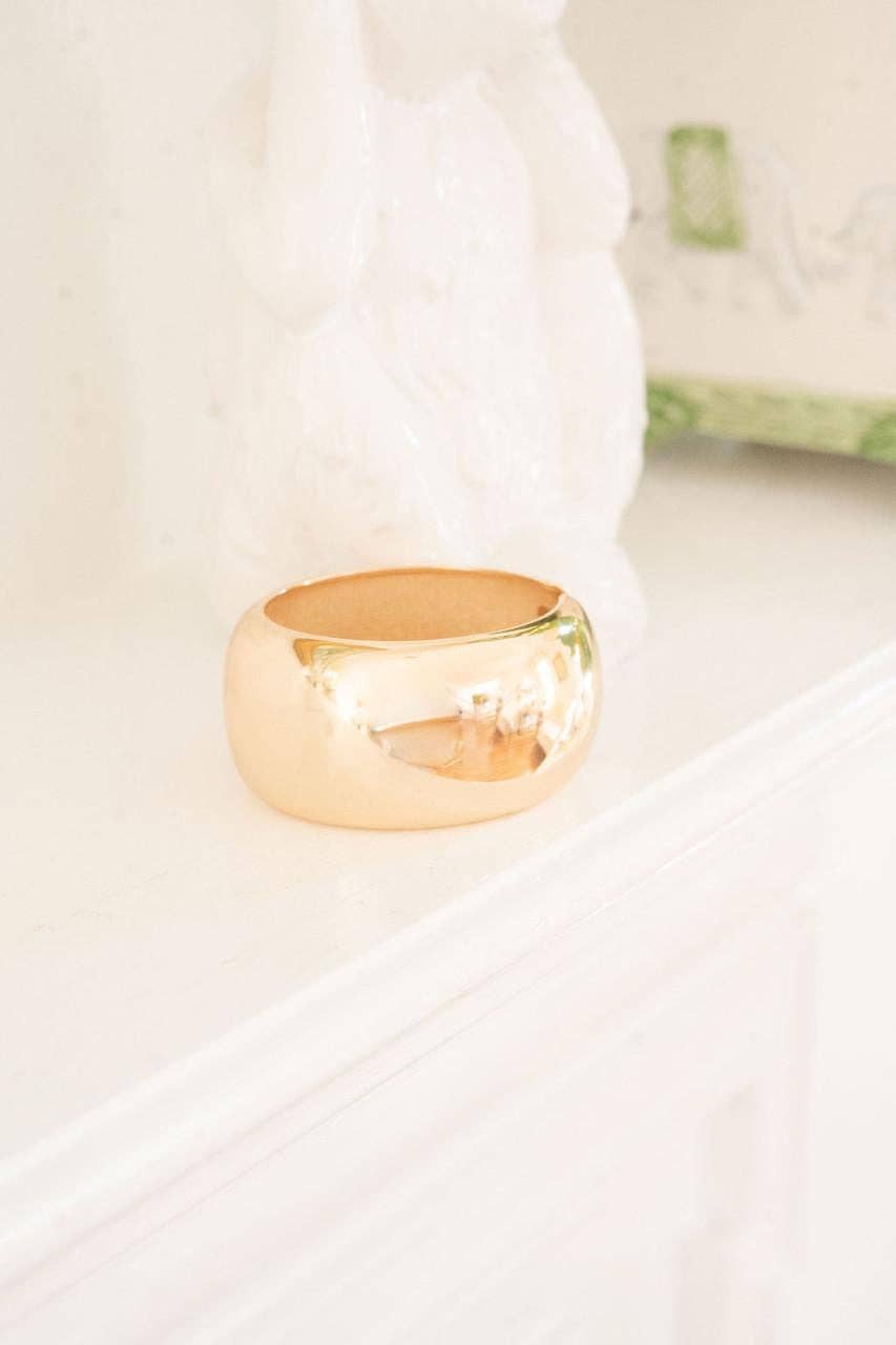 large Gold bangle bracelet on a white surface with a blurred background