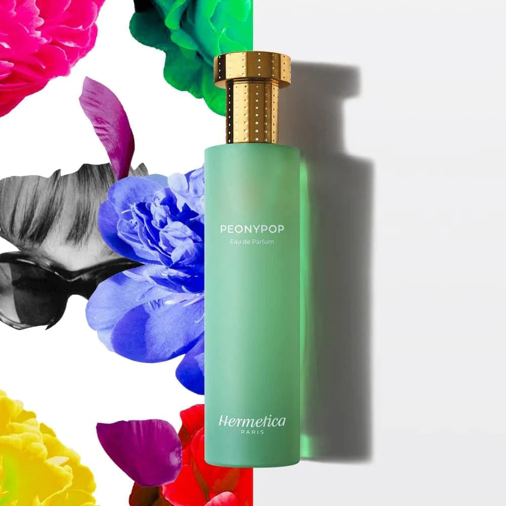 Hermetica clean perfume bottle with gold cap on a white background surrounded by colorful flowers